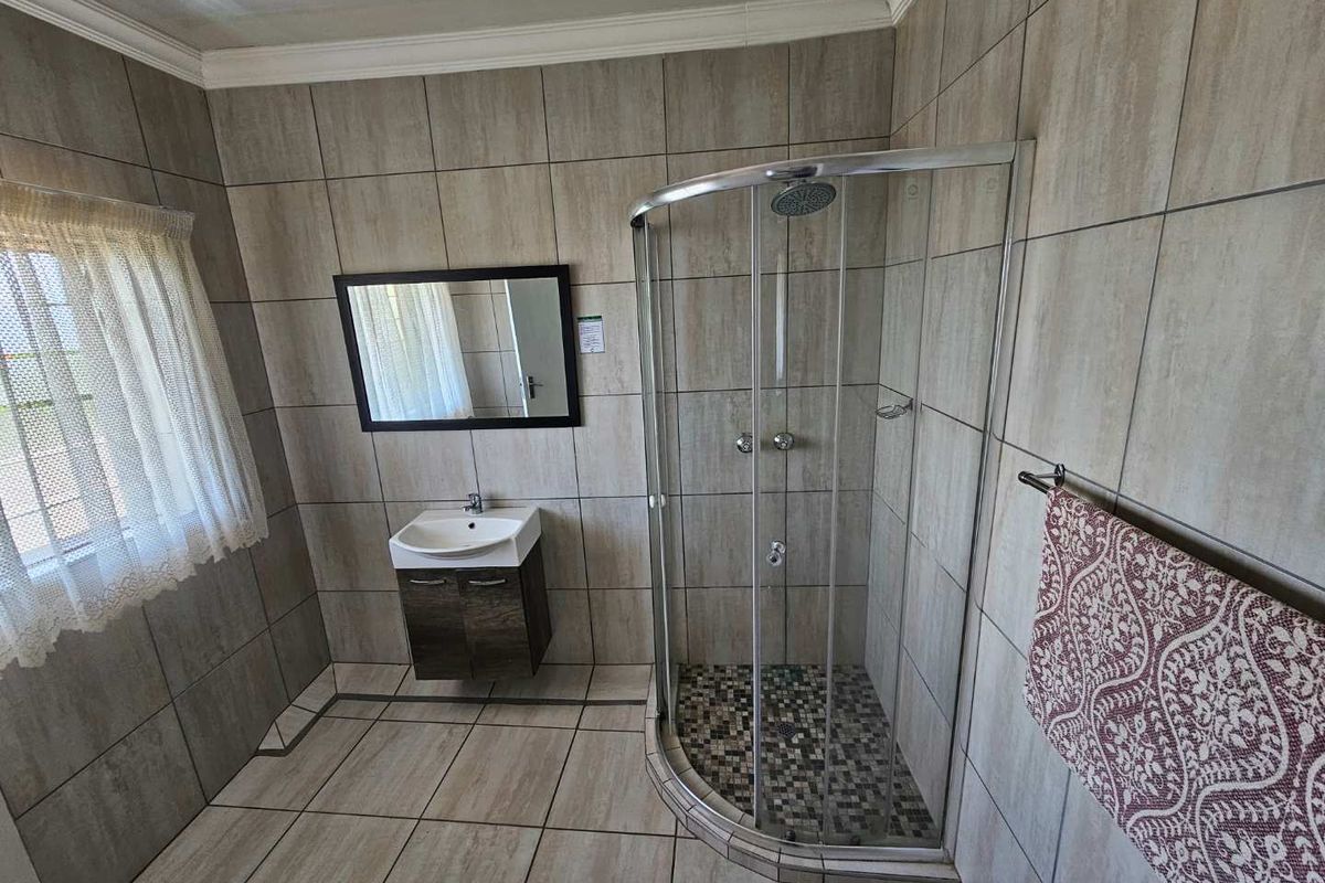 A modern bathroom featuring floor-to-ceiling neutral tiling, a corner glass shower enclosure with mosaic floor detail, and a wall-mounted vanity basin.