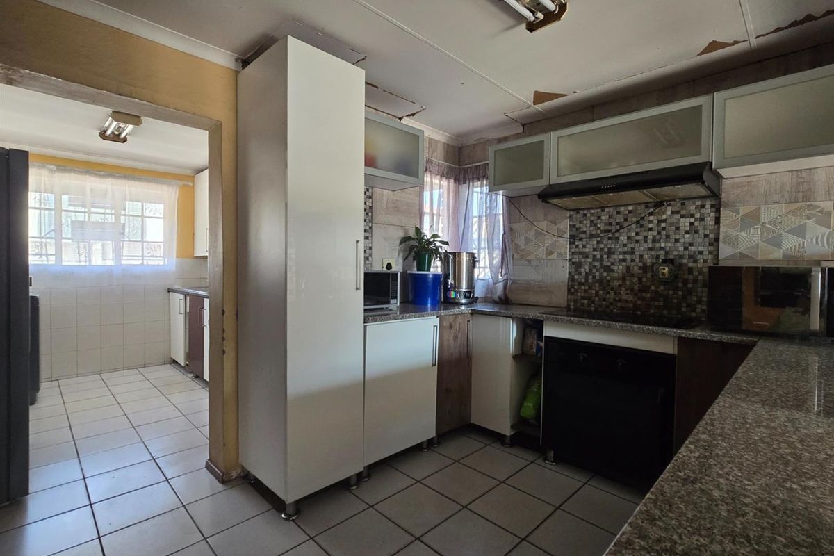 A functional kitchen featuring tiled flooring, built-in cabinetry, a mosaic backsplash, and an integrated extractor fan, with an adjacent utility area visible.