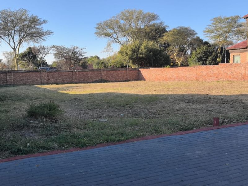 A vacant residential plot featuring a level grassed area enclosed by brick boundary walls and a paved driveway section.