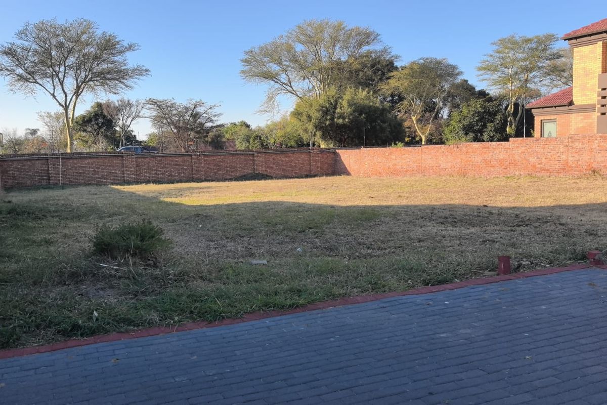 A vacant residential plot featuring a level grassed area enclosed by brick boundary walls and a paved driveway section.
