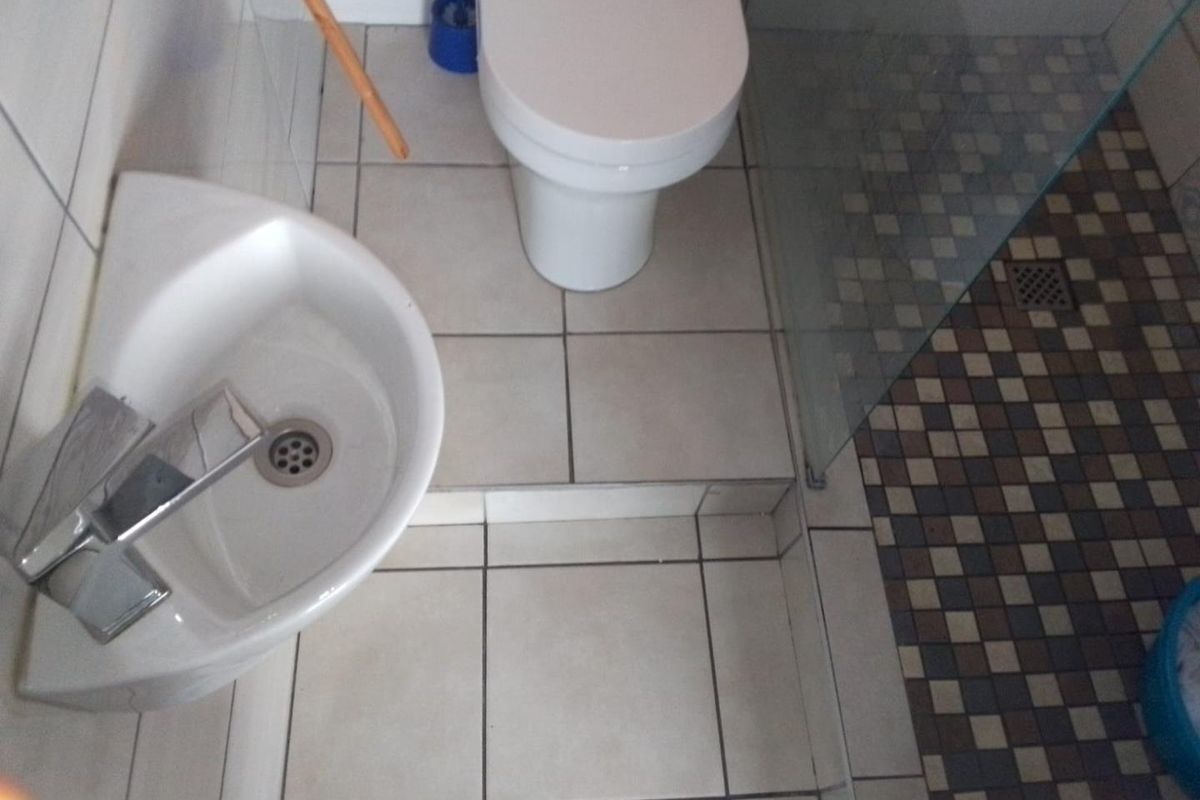 A compact bathroom featuring a wall-mounted basin, toilet, and a walk-in shower with a glass screen and mosaic floor tiling.
