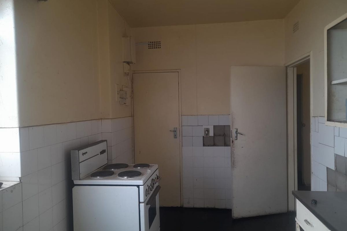A dated kitchen area featuring basic cabinetry, tiled splashbacks, and a freestanding electric stove, requiring renovation to modernize the space.
