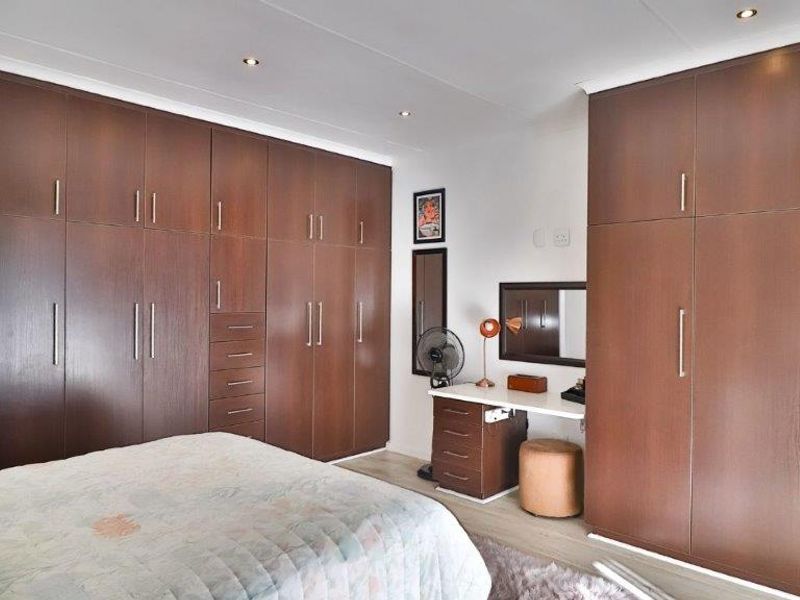 A well-maintained bedroom featuring extensive dark wood built-in cabinetry, recessed ceiling lighting, and light-toned laminate flooring.