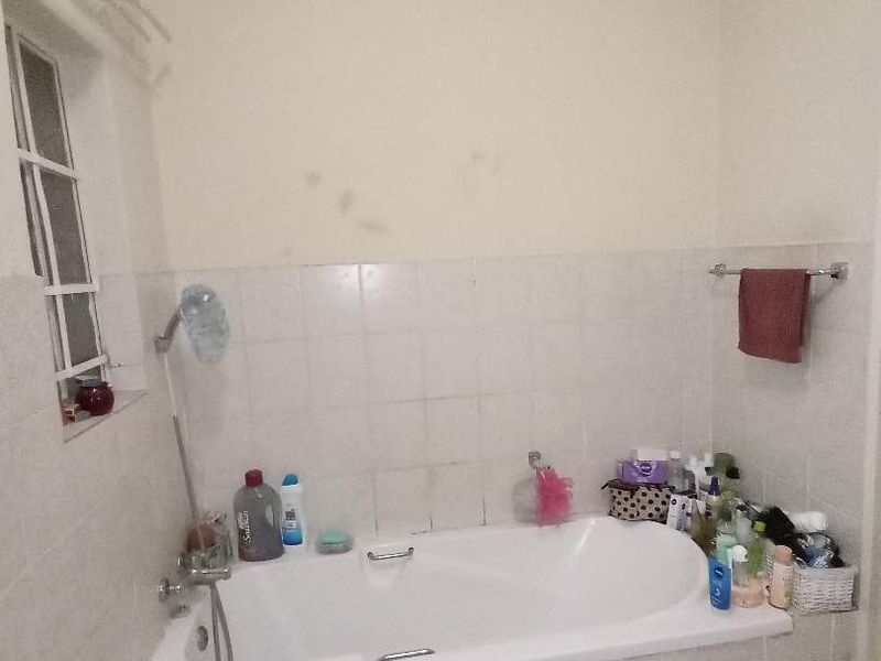 A functional bathroom featuring a built-in bathtub with tiled surround and splashback, tiled flooring, and a window for natural light.