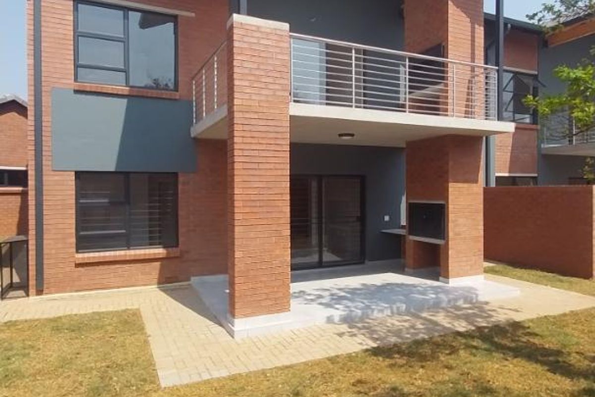 Rear view of a modern townhouse featuring a covered patio with a built-in braai, a balcony, and a private garden area.