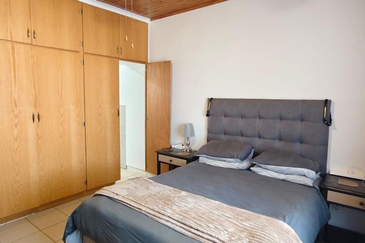A bedroom featuring built-in wooden cupboards, tiled flooring, and a timber-paneled ceiling.