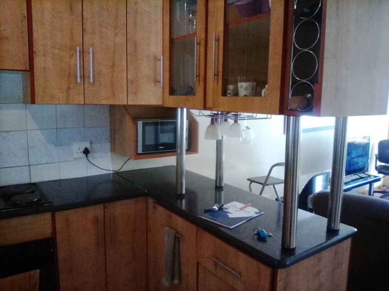 A compact kitchen featuring wood-look laminate cabinetry, dark granite countertops, a built-in microwave, and a breakfast bar with stainless steel supports.