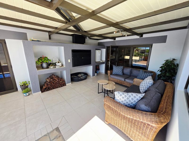 A spacious covered patio featuring a built-in braai, tiled flooring, and exposed beam ceiling, providing an ideal area for outdoor entertaining.