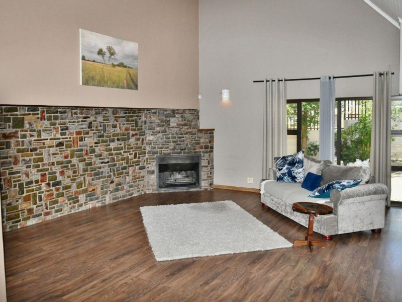 Spacious living room featuring a striking stone-clad fireplace, high vaulted ceilings, and laminate flooring with natural light from large windows and a sliding door.