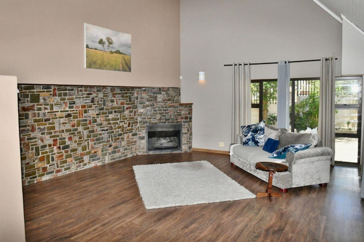 Spacious living room featuring a striking stone-clad fireplace, high vaulted ceilings, and laminate flooring with natural light from large windows and a sliding door.