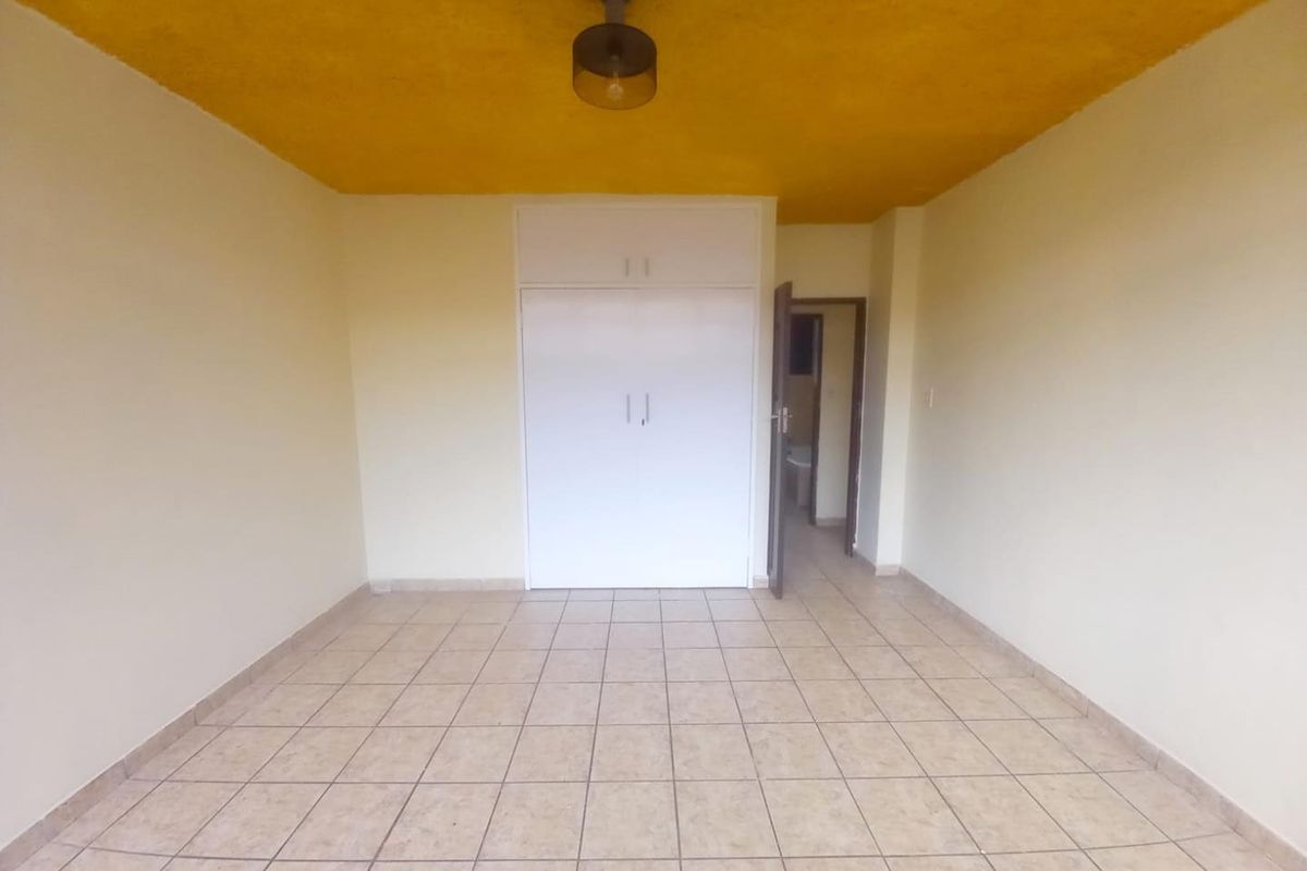 An empty bedroom featuring tiled flooring, a built-in wardrobe, and a distinctive yellow painted ceiling.