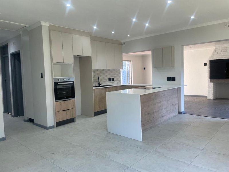 Modern, renovated kitchen featuring a central island, stone countertops, built-in oven, hob, and contemporary cabinetry with a neutral color palette.