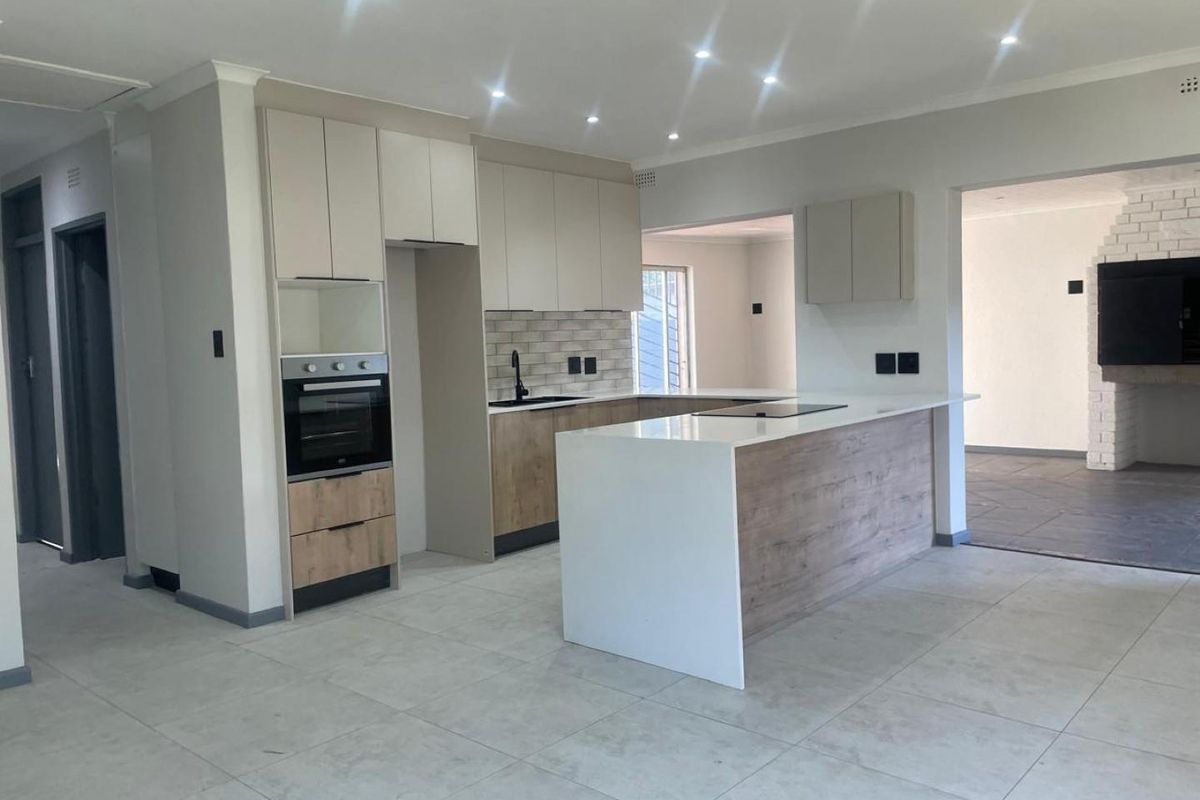 Modern, renovated kitchen featuring a central island, stone countertops, built-in oven, hob, and contemporary cabinetry with a neutral color palette.