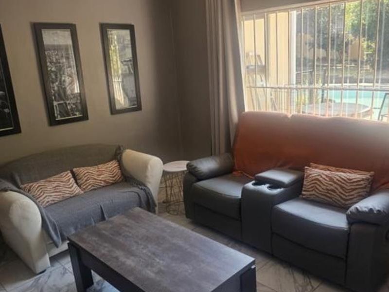 A comfortable living room featuring tiled flooring, neutral wall tones, and large windows fitted with security bars, offering a view of the outdoor area.