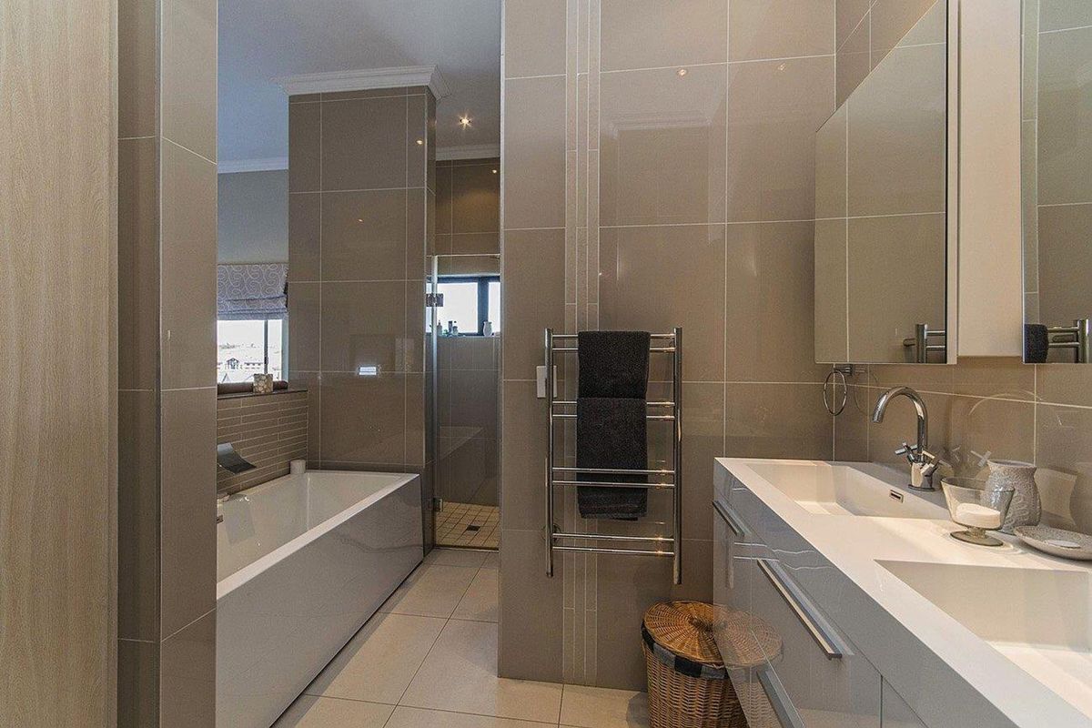 Modern bathroom featuring a double vanity, built-in bathtub, glass-enclosed shower, and a heated towel rail with neutral floor-to-ceiling tiling.