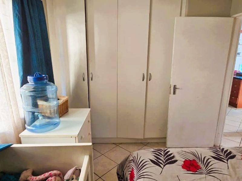 A bedroom featuring built-in cupboards and tiled flooring, with a view into the adjacent living area.