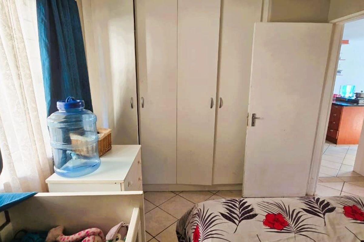 A bedroom featuring built-in cupboards and tiled flooring, with a view into the adjacent living area.