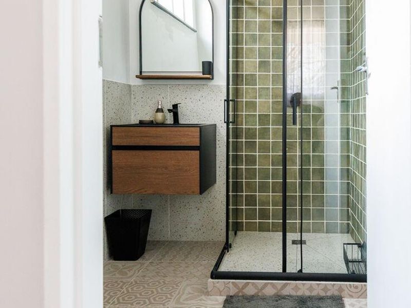 Modern bathroom featuring a walk-in shower with black frame, olive green square wall tiles, patterned floor tiling, and a contemporary wall-mounted vanity unit.