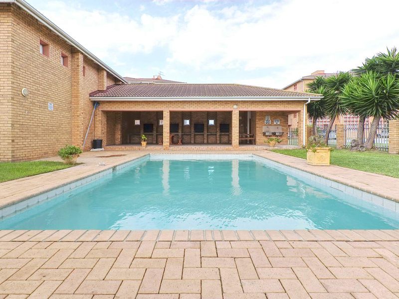 Outdoor pool area featuring a swimming pool, brick paving, and a covered patio with built-in braai facilities.