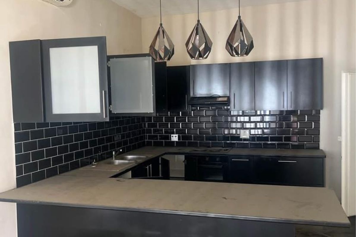 Modern kitchen featuring black cabinetry, subway tile backsplash, integrated oven, hob, extractor fan, and a breakfast bar counter.