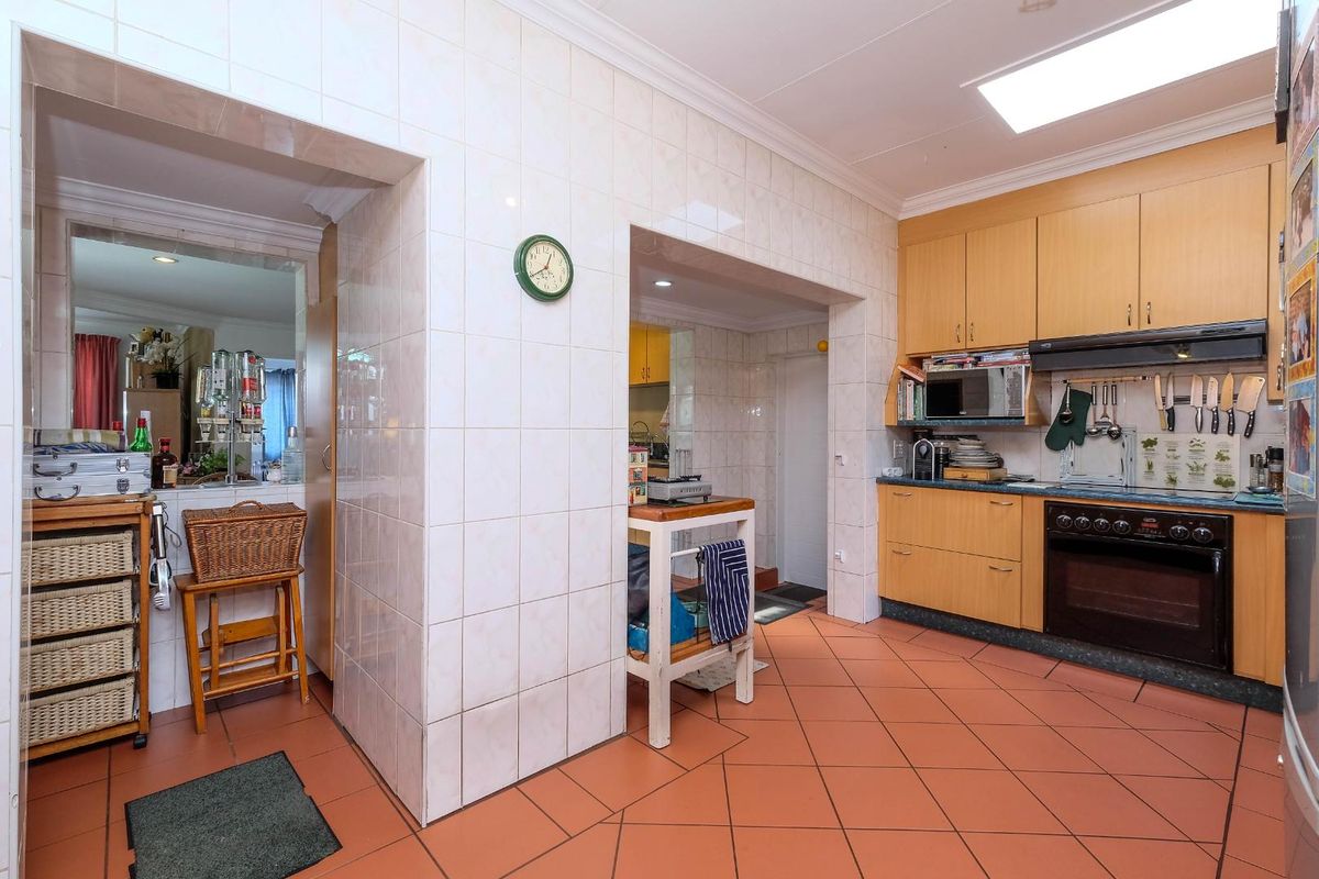 A functional kitchen featuring light wood cabinetry, built-in oven, extractor fan, tiled flooring, and a skylight providing natural light.