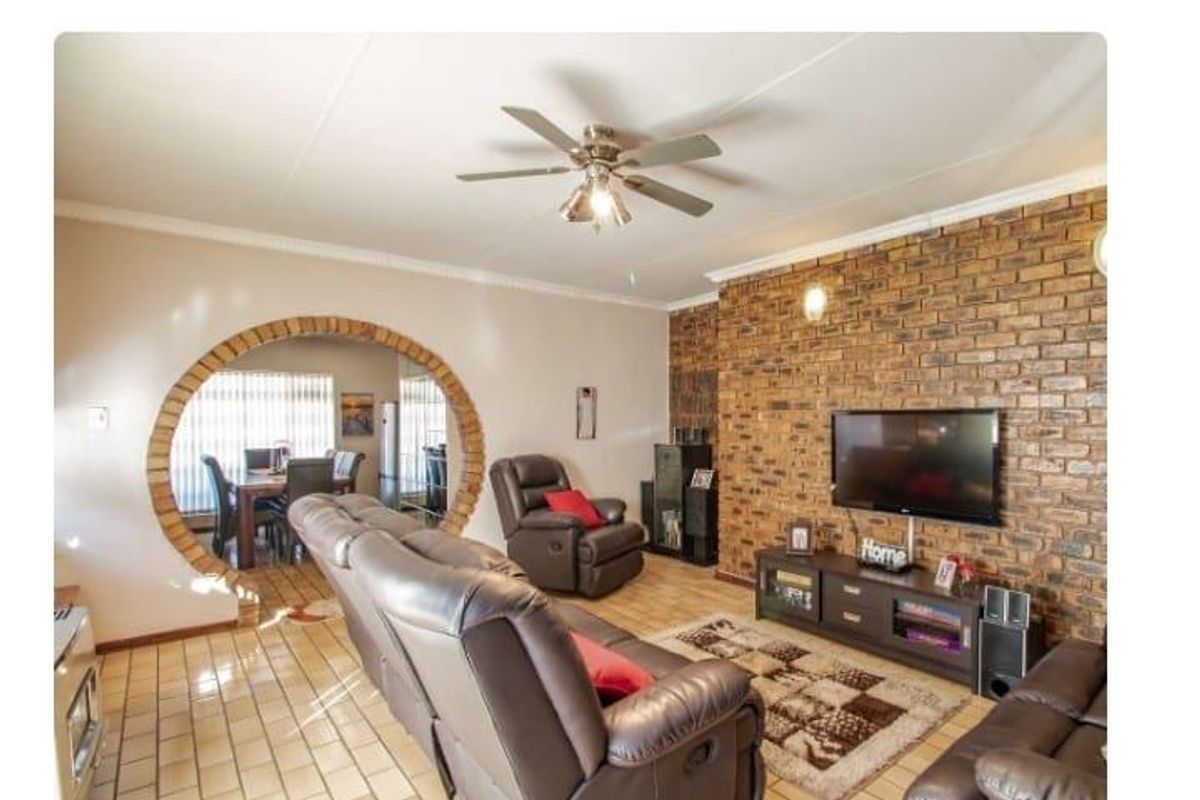 Living room featuring a prominent brick accent wall, tiled flooring, and a distinctive circular archway leading to the dining area.