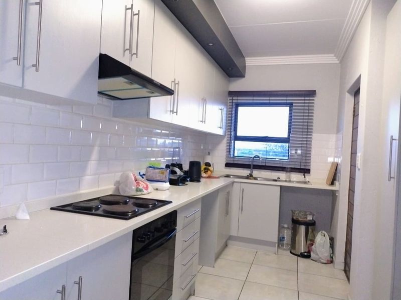 A functional kitchen featuring white cabinetry, subway tile backsplash, integrated electric hob and oven, and tiled flooring with a window for natural light.
