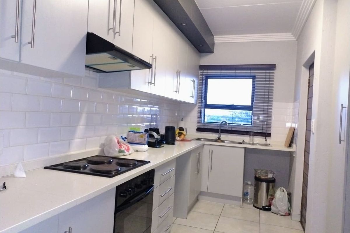 A functional kitchen featuring white cabinetry, subway tile backsplash, integrated electric hob and oven, and tiled flooring with a window for natural light.