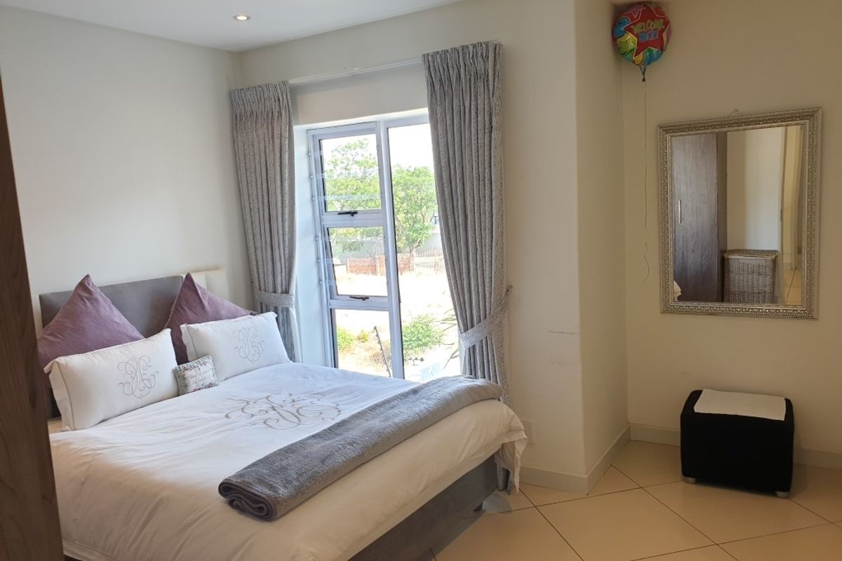 A well-lit bedroom featuring tiled flooring, recessed ceiling lighting, and a large window with curtain tracks.