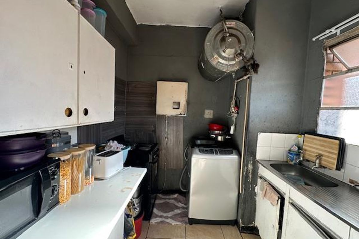 A compact kitchen area featuring built-in cabinetry, a stainless steel sink, and space for laundry appliances, with visible plumbing and electrical infrastructure.