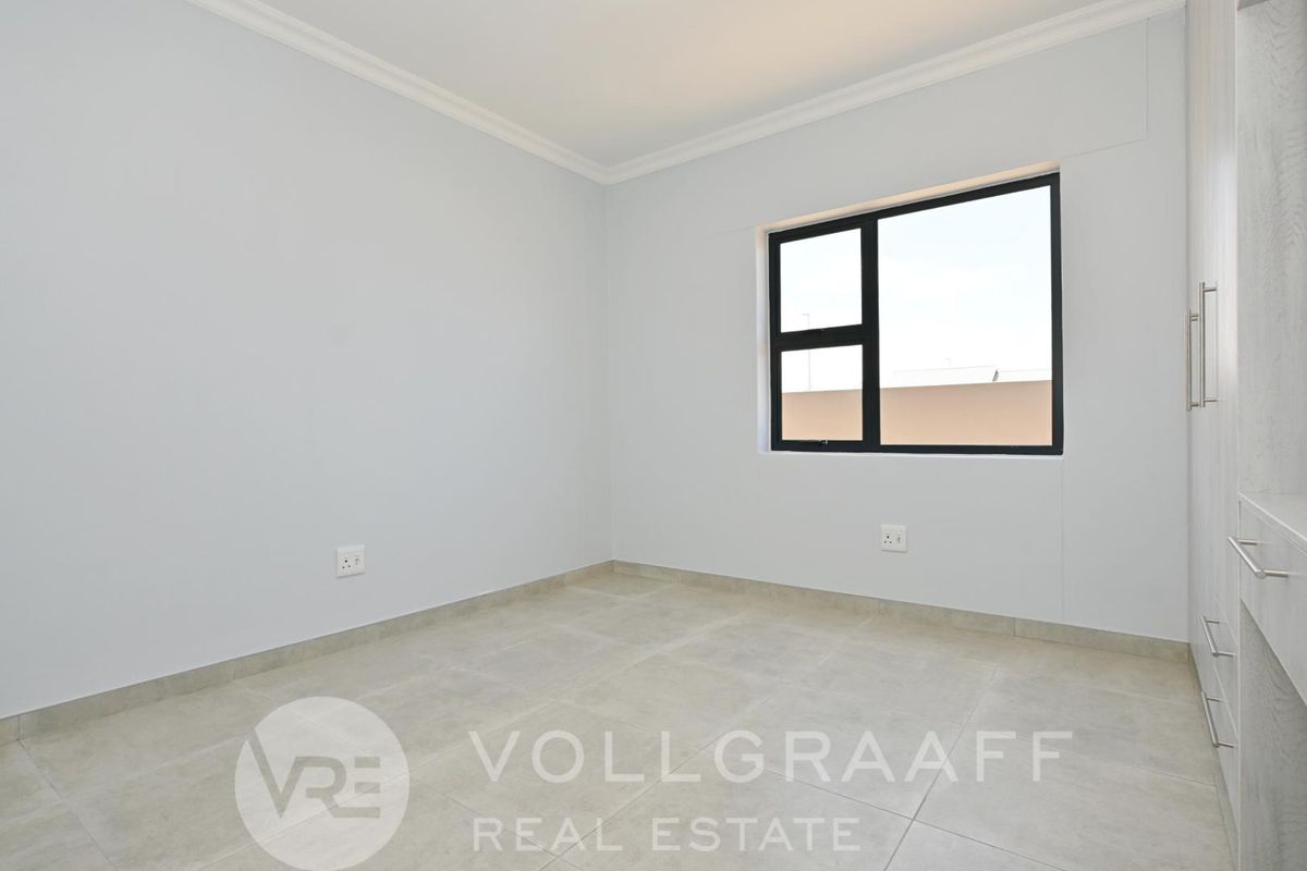 A bright, empty bedroom featuring neutral tiled flooring, modern black-framed windows, and built-in cabinetry.