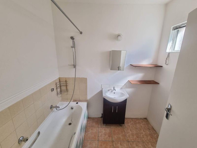 A functional bathroom featuring a bathtub with handheld shower, vanity cabinet with washbasin, and wall-mounted storage shelving.