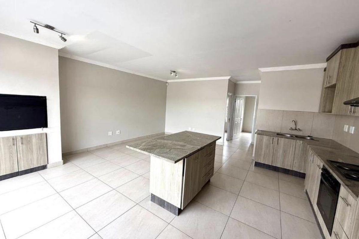 Spacious open-plan living and kitchen area featuring modern laminate cabinetry, a central island, built-in oven, and neutral tiled flooring throughout.