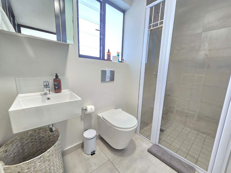 Modern bathroom featuring a wall-mounted basin, wall-hung toilet with concealed cistern, and a glass-enclosed shower with neutral floor-to-ceiling tiling.