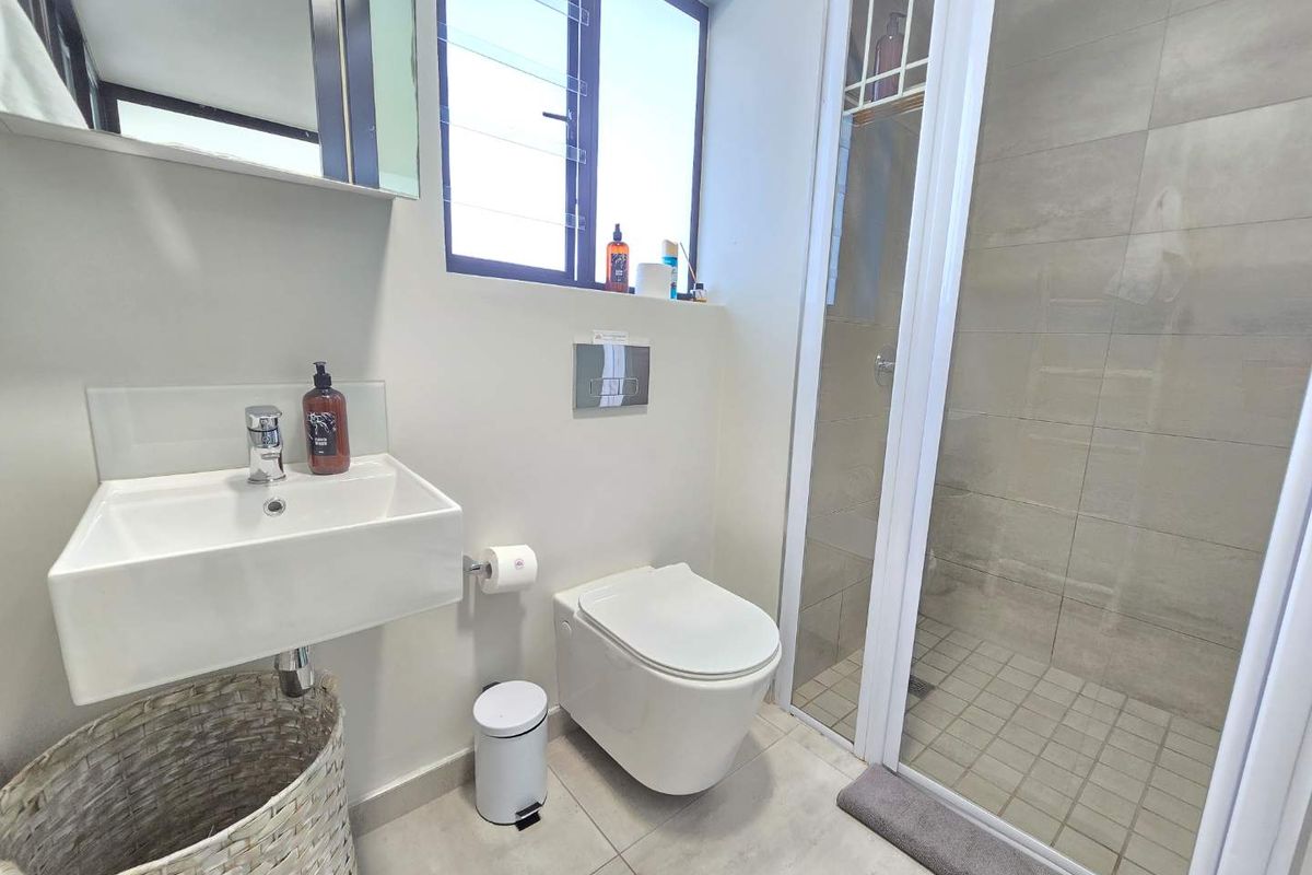 Modern bathroom featuring a wall-mounted basin, wall-hung toilet with concealed cistern, and a glass-enclosed shower with neutral floor-to-ceiling tiling.