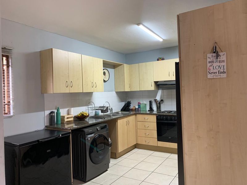 A functional kitchen featuring light wood-finish cabinetry, granite countertops, tiled backsplash, and integrated cooking appliances with tiled flooring.