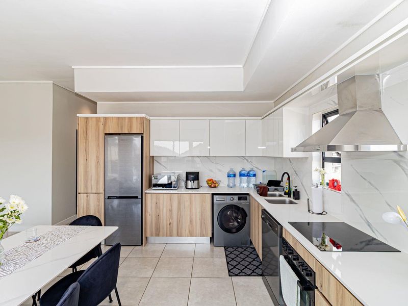 Modern kitchen featuring sleek two-tone cabinetry, stone countertops, marble-look splashback, and high-quality integrated appliances including a hob, oven, and extractor fan.