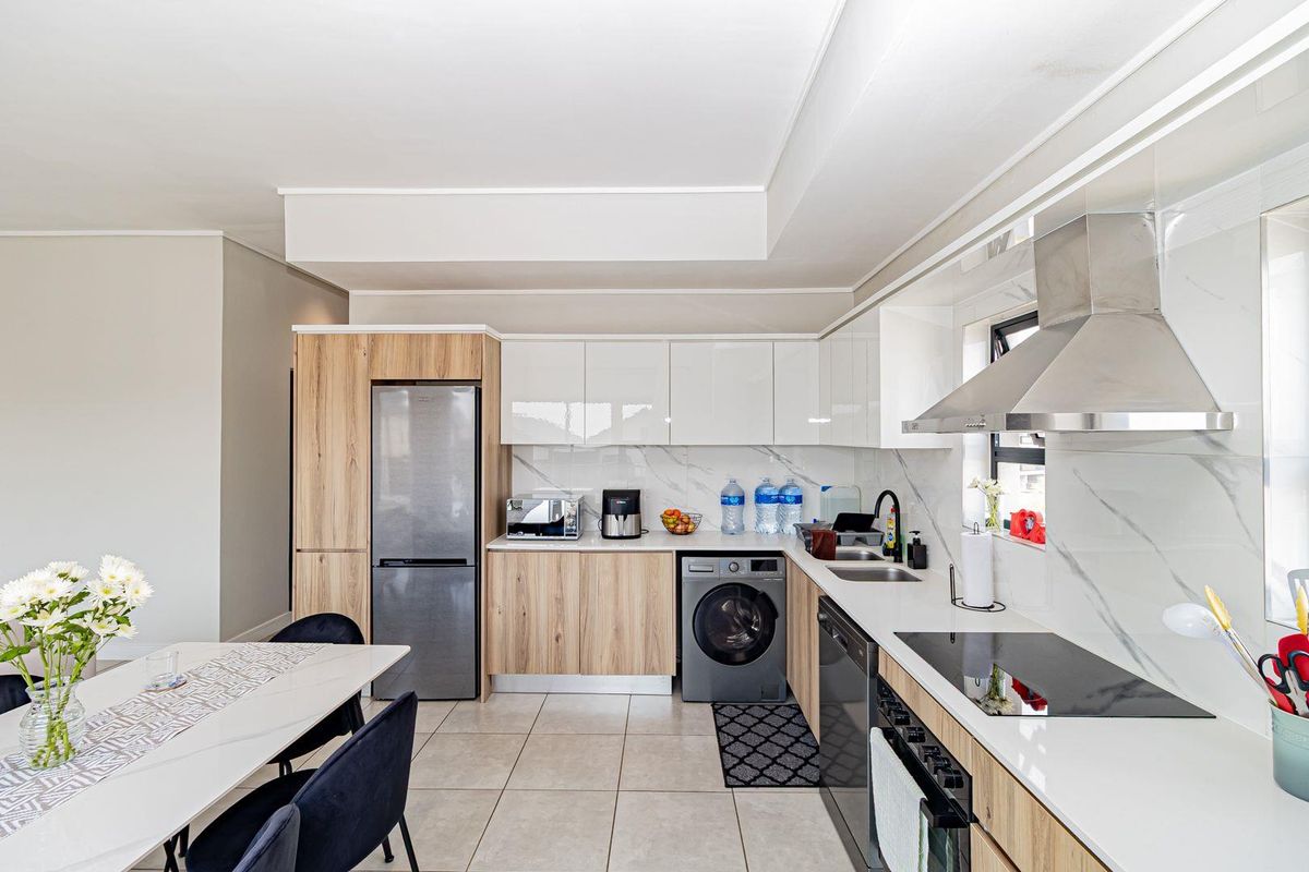 Modern kitchen featuring sleek two-tone cabinetry, stone countertops, marble-look splashback, and high-quality integrated appliances including a hob, oven, and extractor fan.