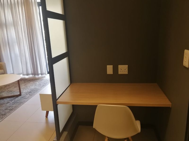 A compact, dedicated home office nook featuring a built-in desk, modern partition screen, and convenient electrical access, integrated into the living area.