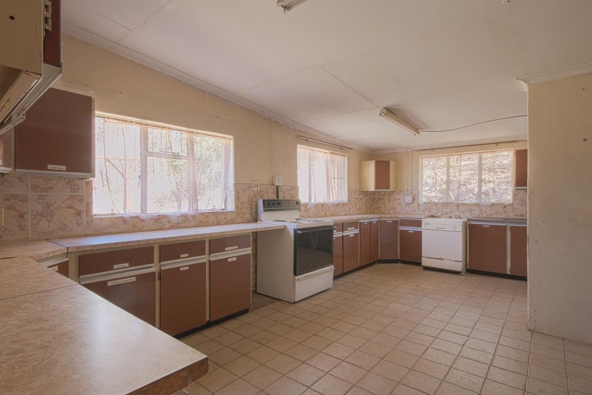 A spacious, dated kitchen featuring original brown cabinetry, tiled countertops, and tiled flooring, offering significant potential for a modern renovation.