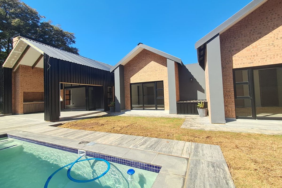 Modern rear exterior featuring a swimming pool, paved deck, and a covered patio area with a built-in braai, set against a contemporary brick facade.