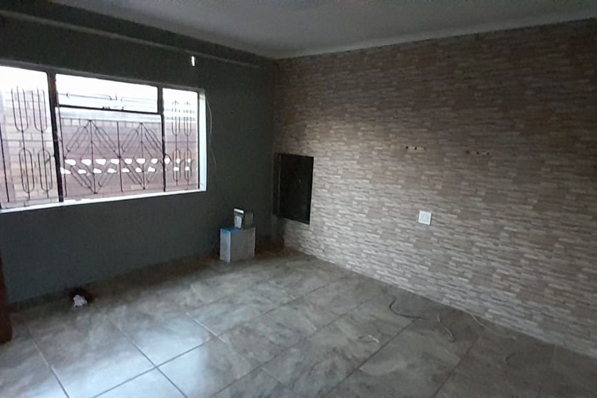 A living room featuring tiled flooring, a textured stone-look feature wall, and security bars on the window.