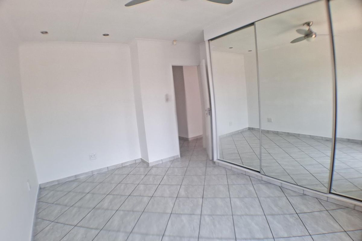 A bright, empty bedroom featuring tiled flooring, recessed downlighting, a ceiling fan, and large built-in mirrored sliding wardrobes.