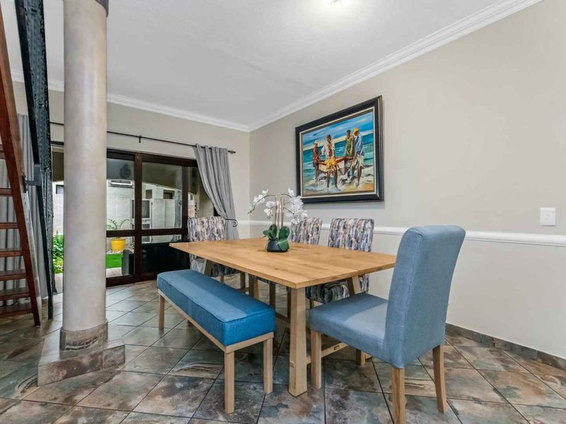 A well-maintained dining area featuring tiled flooring, crown molding, and a wooden staircase, with direct access to the outdoor patio through sliding glass doors.