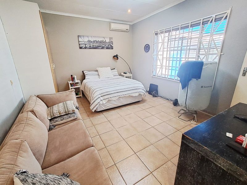 A functional bedroom featuring tiled flooring, a built-in wardrobe, and a wall-mounted air conditioning unit with security bars on the window.