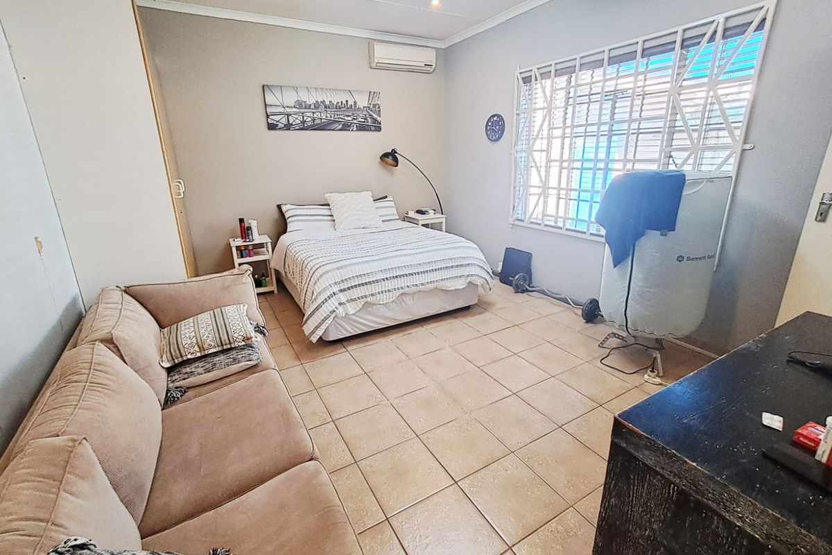 A functional bedroom featuring tiled flooring, a built-in wardrobe, and a wall-mounted air conditioning unit with security bars on the window.