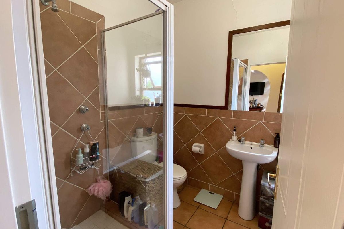 A functional bathroom featuring a shower enclosure, pedestal basin, and toilet with neutral ceramic tiling throughout.
