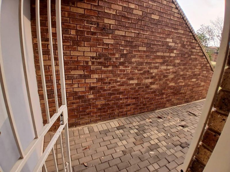 A private rear courtyard area featuring a brick wall and paved flooring, accessible through a metal security gate.