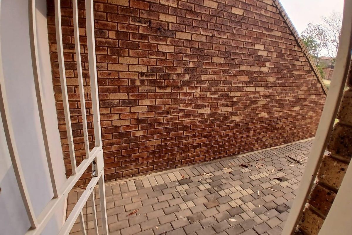 A private rear courtyard area featuring a brick wall and paved flooring, accessible through a metal security gate.