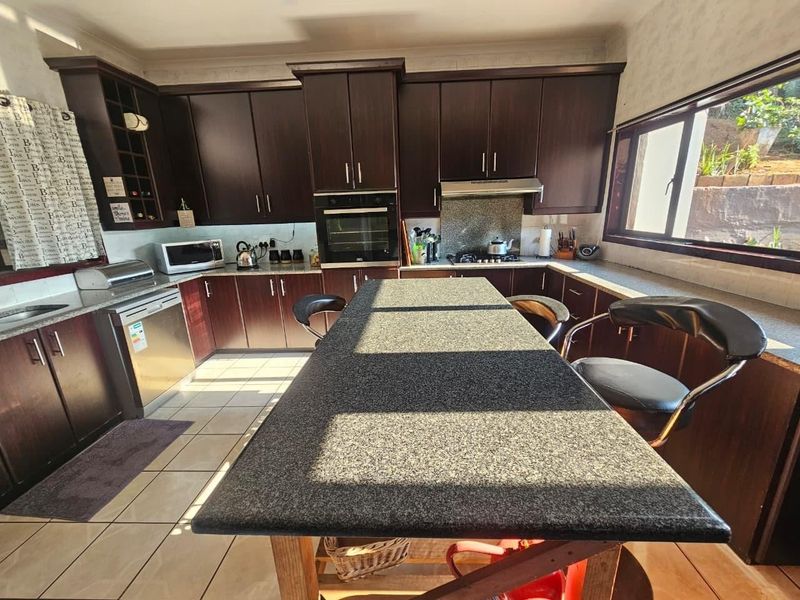 A functional kitchen featuring dark wood cabinetry, granite countertops, a central island, and built-in appliances, offering a classic layout with ample storage space.